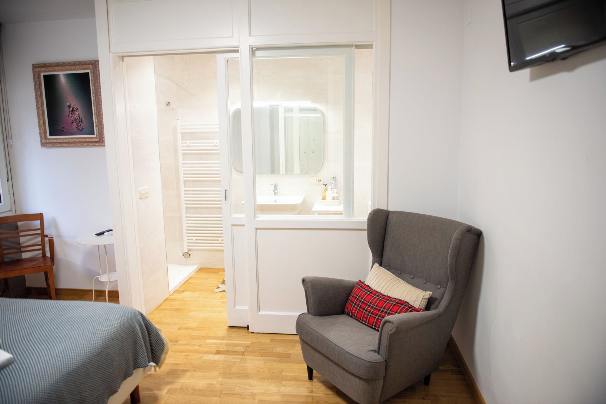 A room with a grey armchair, a bed with a blue blanket, a small table, and a white radiator.