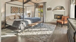 Ein Raum mit einem Himmelsbett, einer Bank, einem Kamin und einem Deckenventilator, verziert mit Holzbalken und einem großen Fenster.