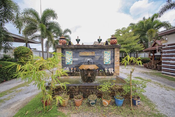 A stone fountain with water spouting from the center, surrounded by potted plants and palm trees.