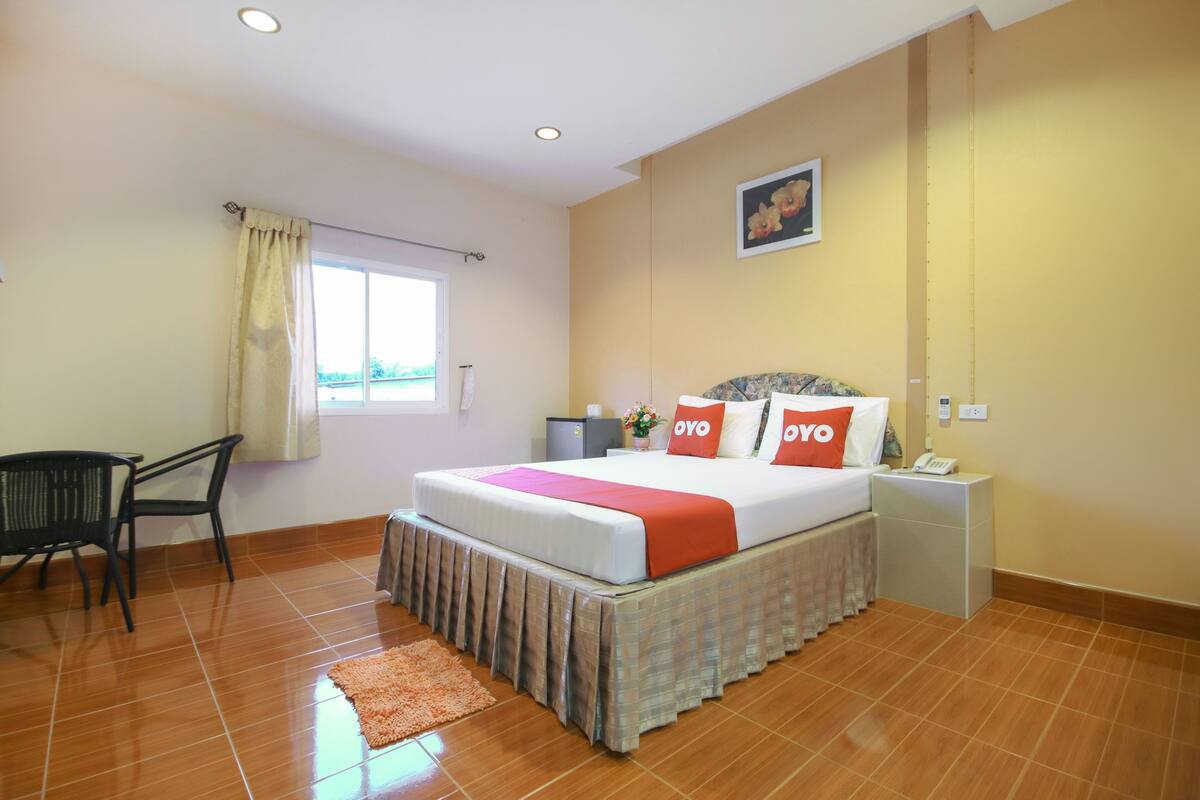A hotel room with a bed, a desk, a chair, a nightstand, and a window with curtains.