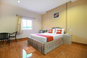 A hotel room with a bed, a desk, a chair, a nightstand, and a window with curtains.