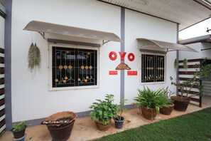 A building with a sign reading "OYO" and two windows with decorative grills. There are several potted plants in front of the building.
