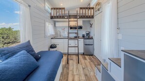 Uma cabana compacta e moderna, com um quarto no mezanino, uma cozinha compacta e uma grande janela com vista para o exterior.