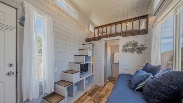 Quarto compacto com beliche, estantes embutidas, sofá azul e uma pequena janela.