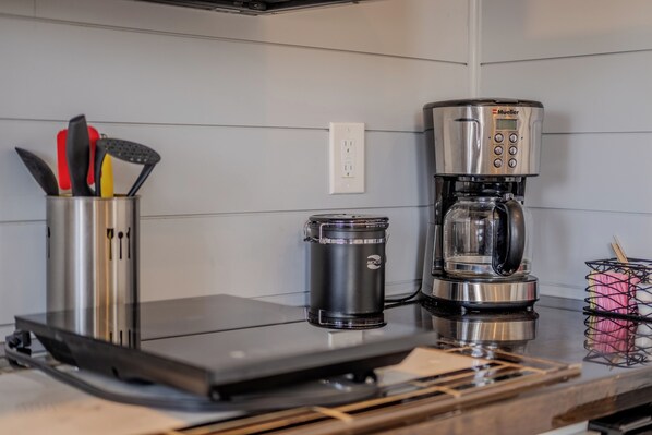 Uma cozinha com cafeteira, um recipiente e utensílios.
