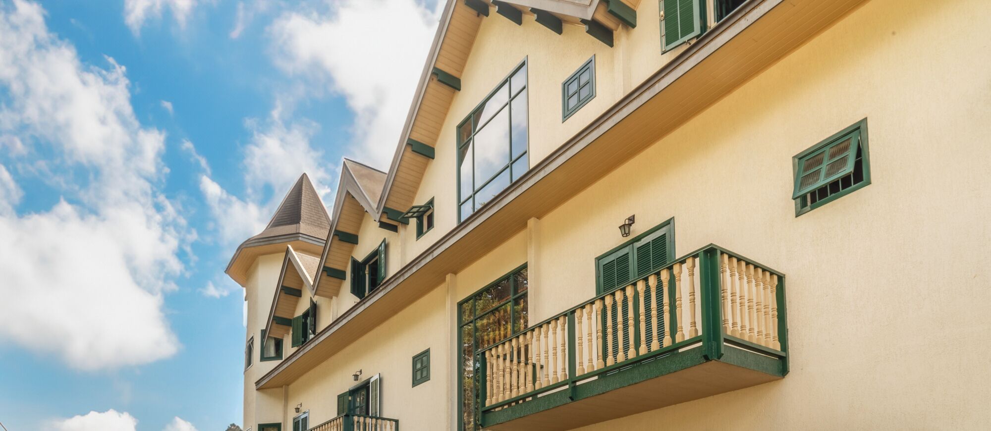 A multi-story building with a yellow facade, green shutters, and a balcony with a balustrade.