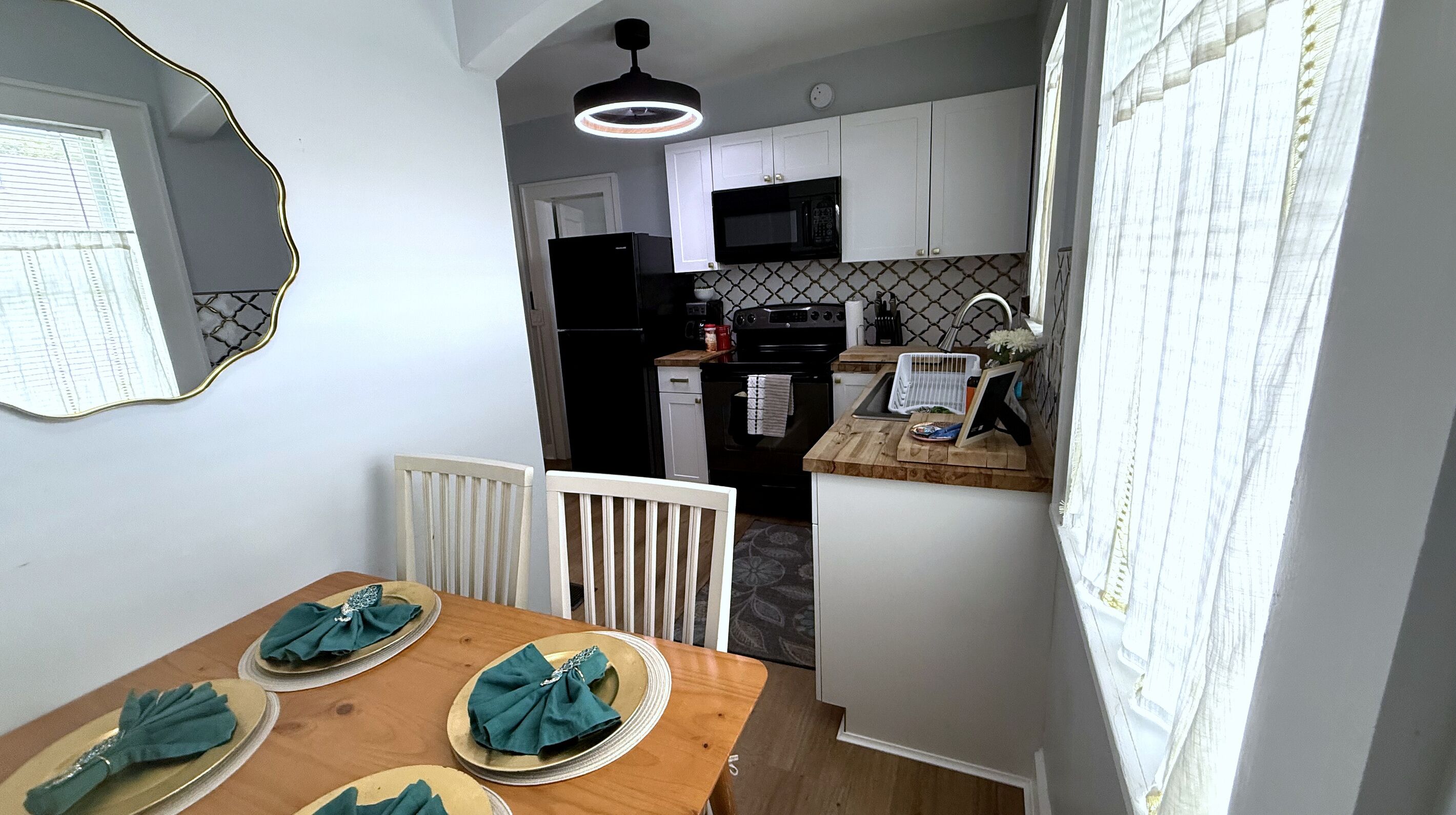 Un comedor con una mesa preparada para cuatro, un radiador blanco y una cocina con armarios blancos y un microondas negro.
