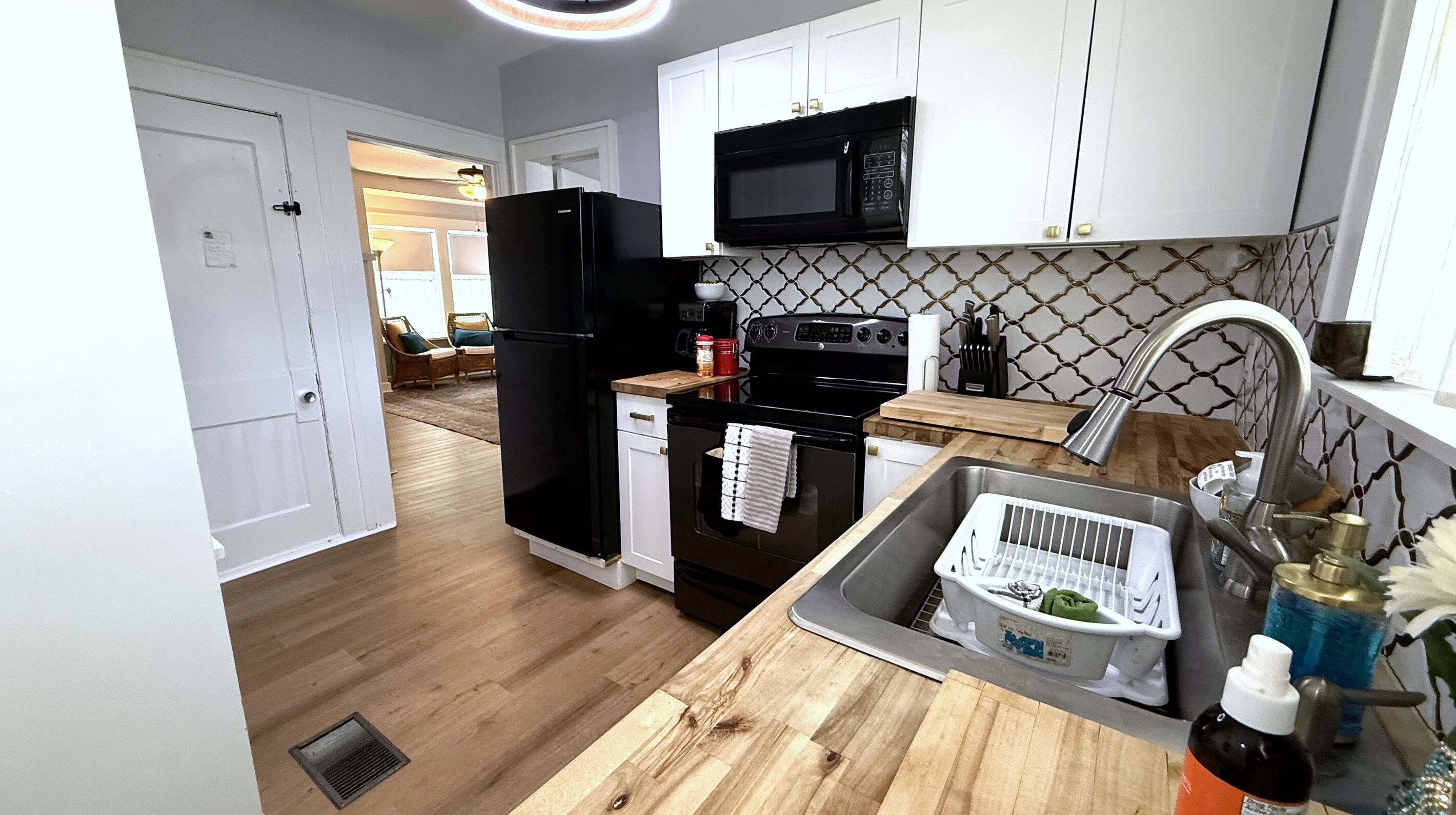 A kitchen with white cabinets, a black refrigerator, a microwave, a stove, and a sink with a dish rack.