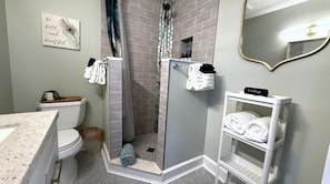 A bathroom with a toilet, shower, sink, and a towel rack.
