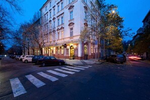 A multi-story hotel with a classic architectural style, featuring a prominent entrance and a parking area in front. - Aron (Prague)