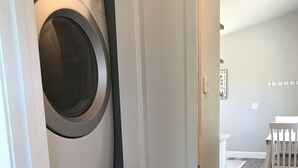 A laundry room with two stacked front-loading washing machines and a white door leading to another room. - Cozy 1 bedroom with beautiful Alaskan views (Anchorage)