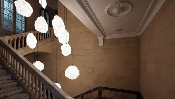 A grand staircase with a balustrade, a stone wall, and a ceiling with a decorative medallion. - Basic Hotel (Olerdola)
