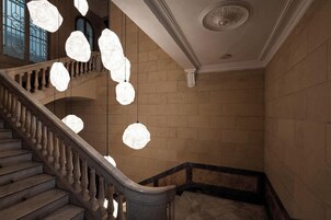 Una imponente escalera con barandilla, pared de piedra y techo decorado con una medalla ornamental.