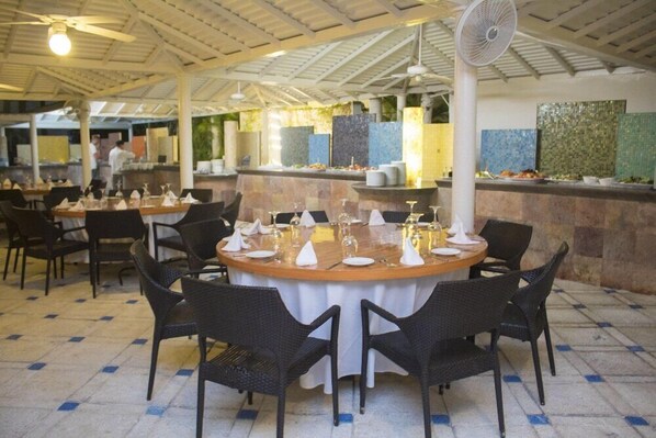 En restaurant med runde borde, et barområde og en ventilator i loftet.