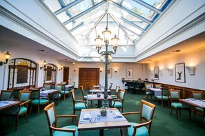 A restaurant with a high ceiling and skylight, wooden tables and chairs, and framed artwork on the walls. - Opera Antiaging and Spa (Sopot)