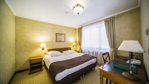 Una habitación de hotel con una cama grande, dos lámparas de noche, un escritorio con lámpara y una ventana con cortinas.