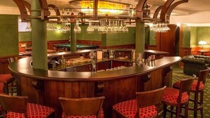 Una zona de bar con mostrador curvo, numerosos vasos colgantes y sillas con acolchado rojo.