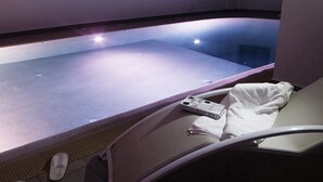Wellnessbereich mit Whirlpool, Handtuch, Hausschuhen und Fernbedienung auf einem Sessel.