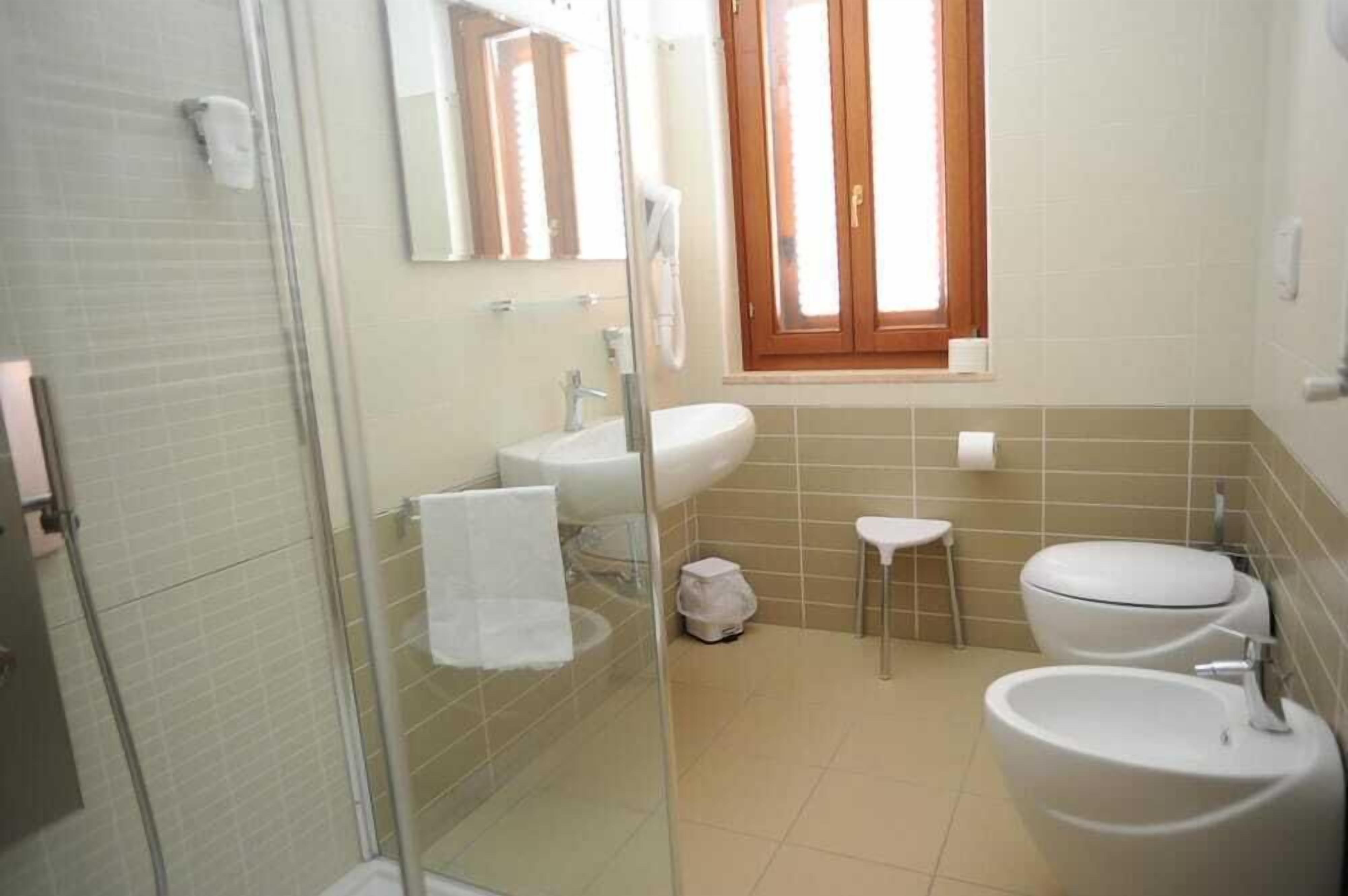A bathroom with a glass shower enclosure, a sink, a toilet, and a window with wooden shutters.