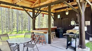 Un espacio al aire libre techado con mesas y sillas, una barra y una estación de parrillada.
