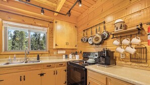 Cocina de cabaña de madera con un ventanal grande, armarios de madera, estufa y ollas y tazas colgando.