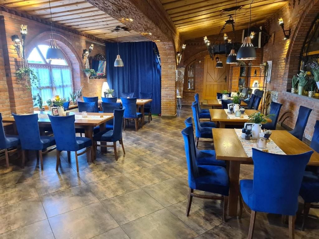 A restaurant with brick walls, wooden beams, and blue upholstered chairs. Tables are set with plates, cups, and cutlery.