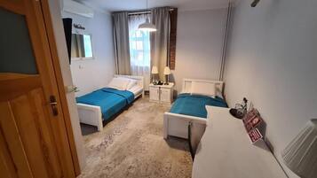 Une chambre d’hôtel avec deux lits simples, un bureau, une chaise, une lampe, un radiateur et une porte.