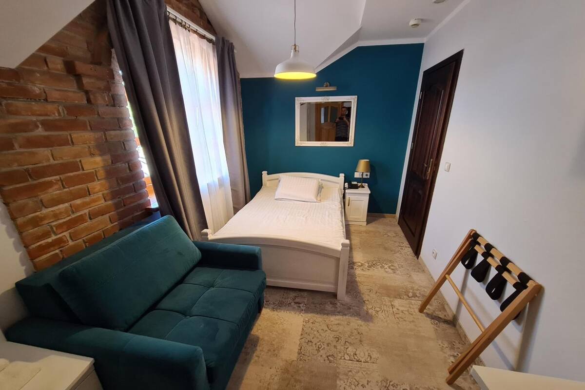 Une chambre à coucher avec un lit, un canapé vert, une armoire en bois, une table de chevet, un miroir et une fenêtre avec des rideaux.