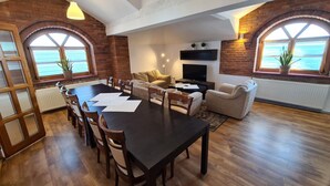 A spacious living area with a dark wooden dining table, comfortable seating, and large windows with a view. - Hotel Staropolski (Tomaszow Lubelski)