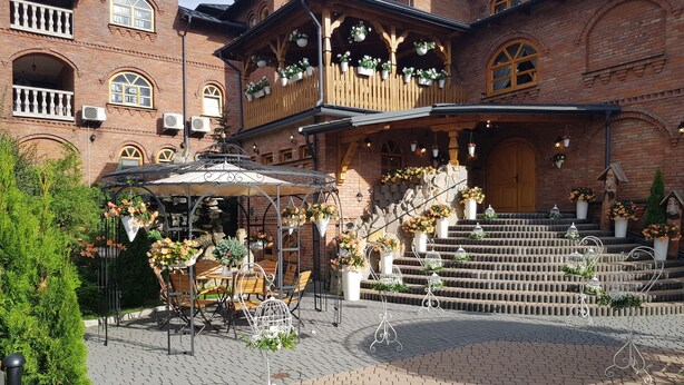 A traditional building with a wooden balcony, a stone staircase, and a garden area with a table and chairs. - Hotel Staropolski (Tomaszow Lubelski)
