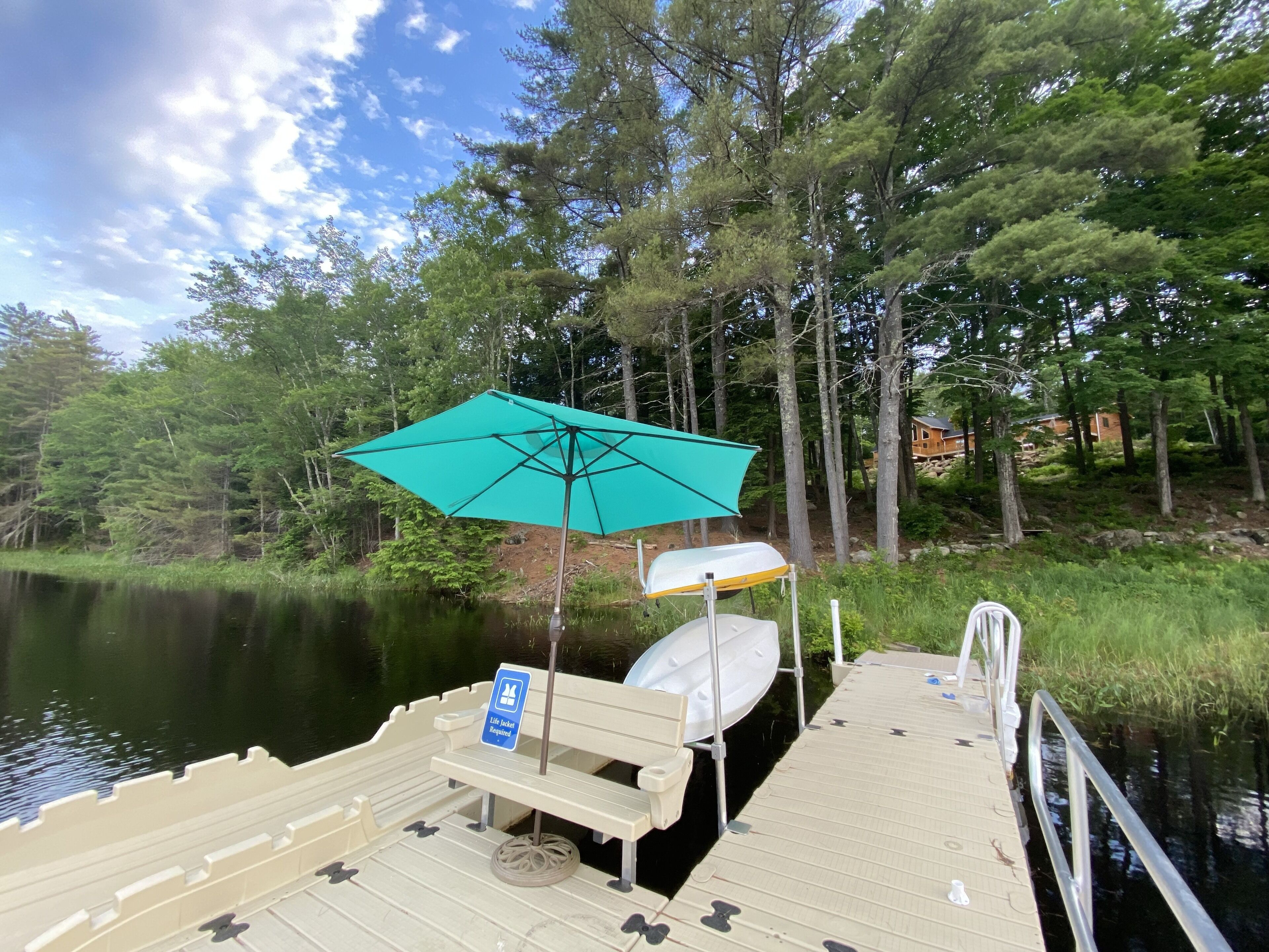 A dock with a bench, a boat, and a turquoise umbrella.