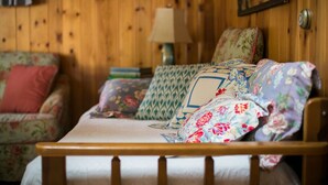 Ein Zimmer mit Holzwänden, einem Bett, einem sofa mit Blumenmuster und einer Lampe.