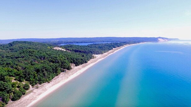 Luftaufnahme einer Küstenlandschaft mit Sandstrand, dichtem Wald und blauem Meer.