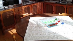 A kitchen with wooden cabinets, a stove, a sink, and a dining table with a placemat. - B&b Aloysia - Regalati una Vacanza!!!! (Iglesias)
