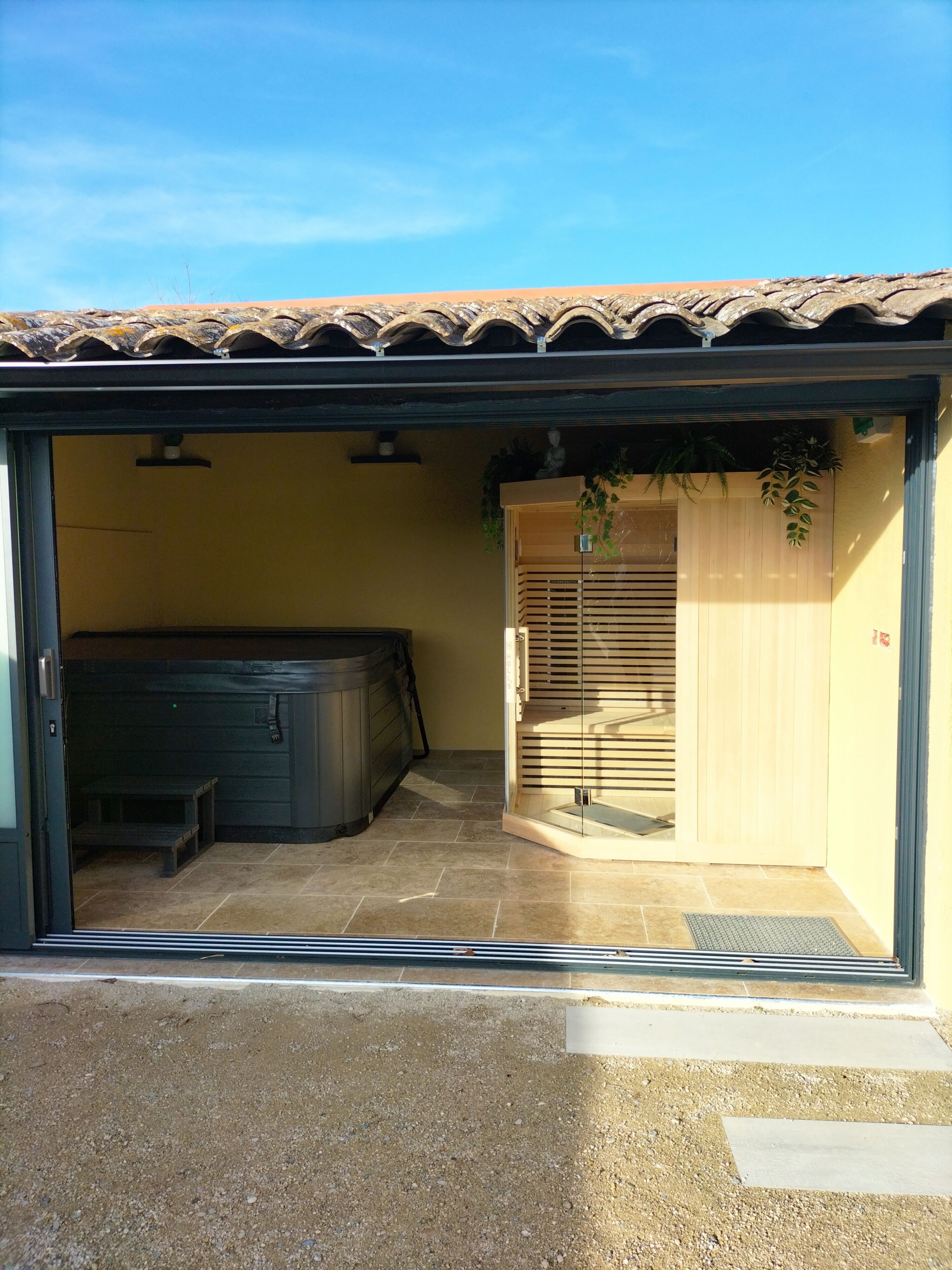 Een overdekt buitengebied met een jacuzzi, een houten deur en een betegelde vloer.