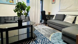A modern living room with a sofa, a dining table, and a potted plant. - Atom Large 4/5 Bed House, Balcony, Sleeps 13, Free Parking, East London (Barking)