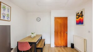 A small, bright room with a wooden table, a clock, and a door. - Atom Large 4/5 Bed House, Balcony, Sleeps 13, Free Parking, East London (Barking)