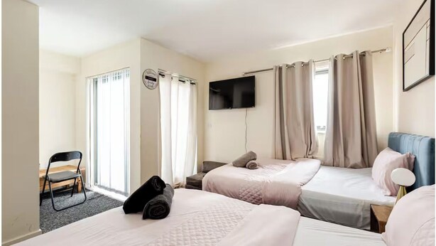 A hotel room with two beds, a TV, and a chair. - Atom Large 4/5 Bed House, Balcony, Sleeps 13, Free Parking, East London (Barking)