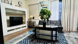 A modern living room with a flat-screen TV, a sofa, a coffee table, and a potted plant. - Atom Large 4/5 Bed House, Balcony, Sleeps 13, Free Parking, East London (Barking)