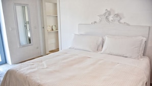 A neatly made bed with a white headboard and two pillows, a mirror on the wall, and a door leading to a bathroom. - Borgo S. Clara - Maria by Wonderful Italy (Cisternino)