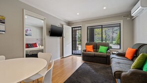 A modern living room with a sofa, a dining table, and a TV. - Grevillea Gardens Unit 5 (BRIGHT)