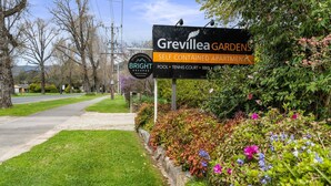 A sign for Grevillea Gardens, a self-contained apartment complex with amenities like a pool, tennis court, BBQ, and free Wi-Fi. - Grevillea Gardens Unit 5 (BRIGHT)