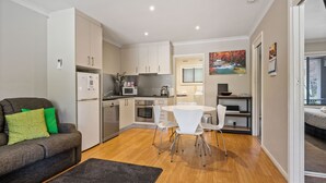A compact living space with a kitchenette, a dining area, and a sofa with cushions. - Grevillea Gardens Unit 5 (BRIGHT)