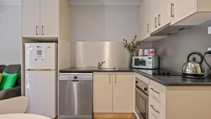 A compact kitchen with a dishwasher, microwave, kettle, and a sink. - Grevillea Gardens Unit 5 (BRIGHT)
