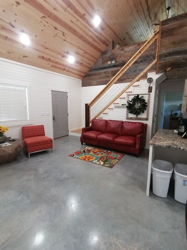 A spacious living area with a red leather couch, a wooden staircase, and a decorative wreath on the wall.