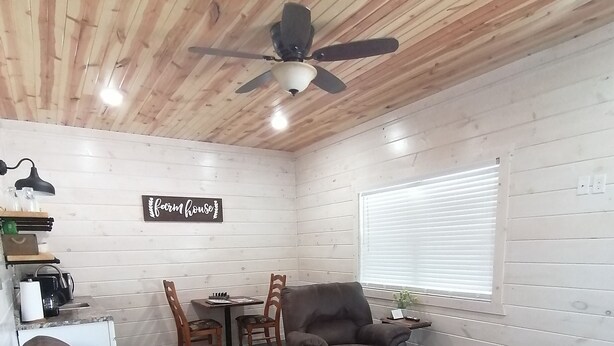 Un salon chaleureux avec un canapé en cuir marron, un plafond en bois, un ventilateur de plafond et un panneau décoratif représentant une ferme accroché au mur.