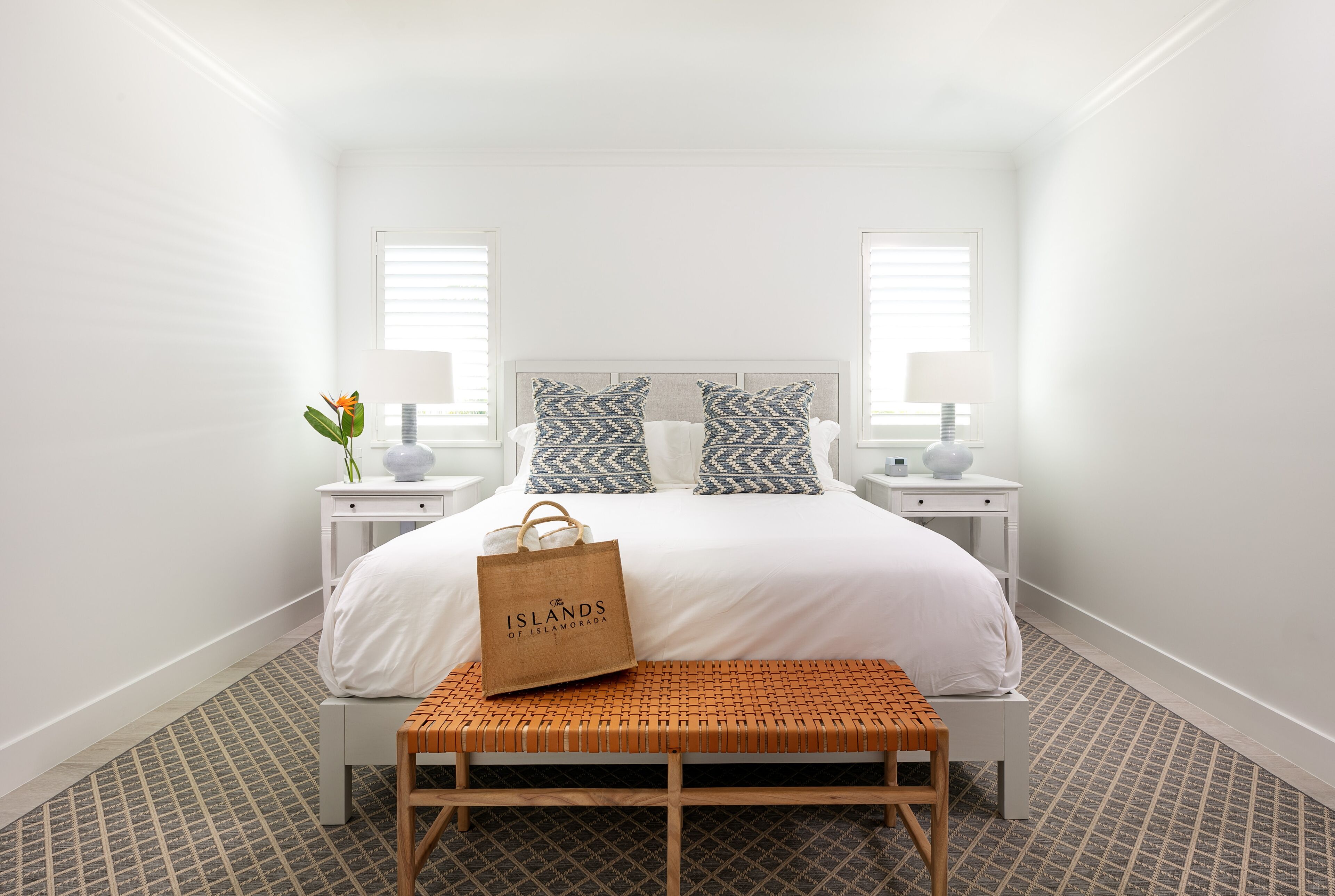 A neatly arranged bedroom with a bed, two bedside tables, a bench, and a bag.