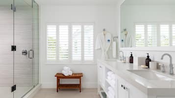 Une salle de bain moderne avec une douche à parois de verre, un banc en bois, un grand miroir et un meuble-lavabo blanc avec un évier.