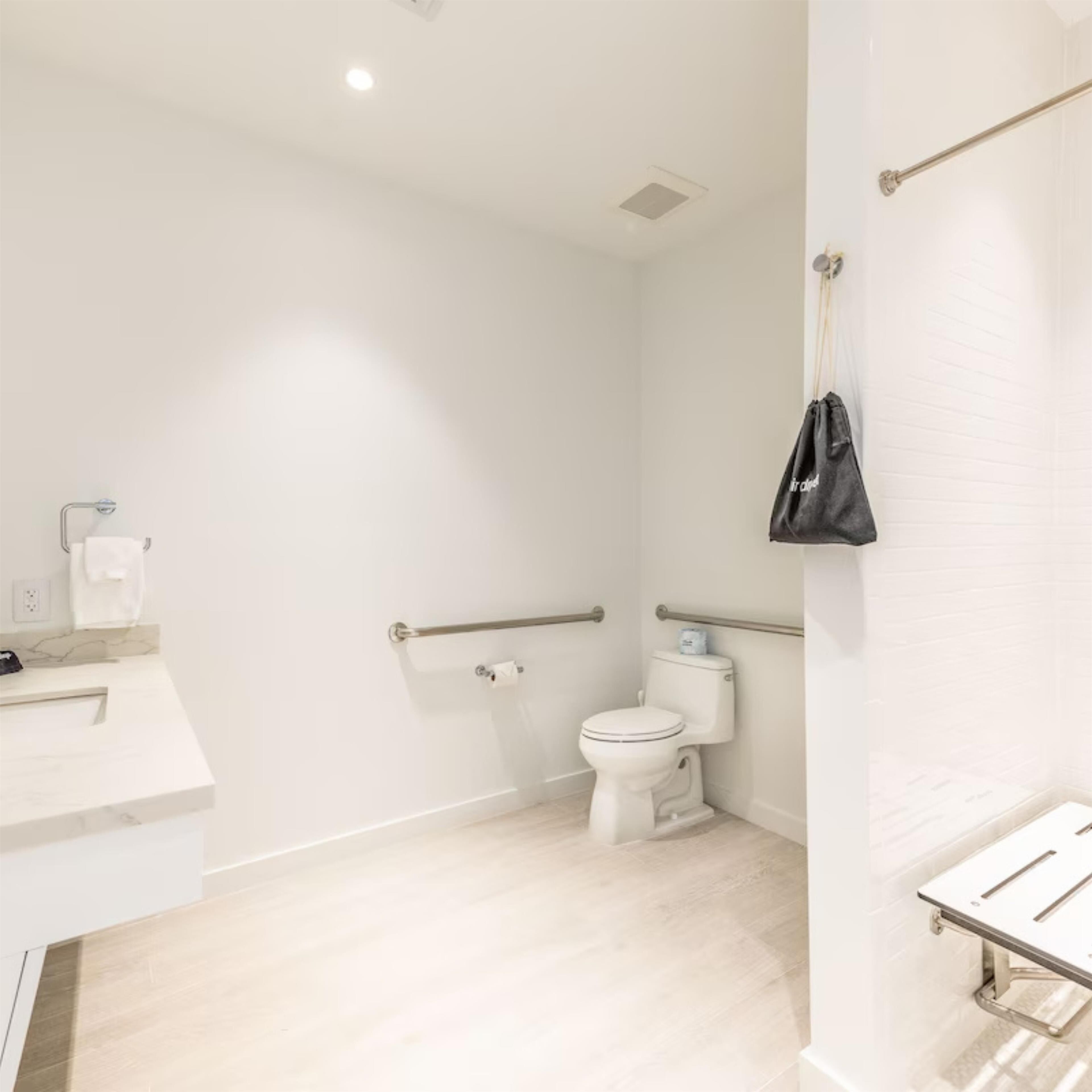Une salle de bain moderne équipée de toilettes, de barres d’appui, d’un lavabo et d’un porte-serviettes.