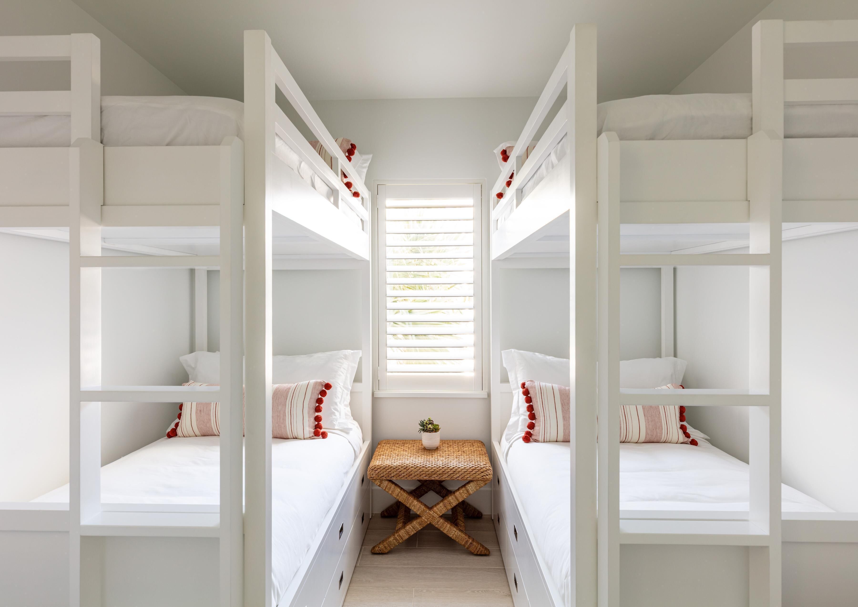 A room with bunk beds, a small table, and a window with blinds.